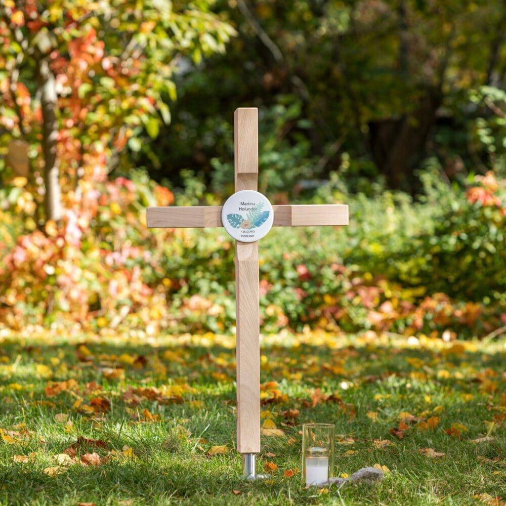 Helles Grabkreuz mit rundem, farbig gestaltetem Grabschild